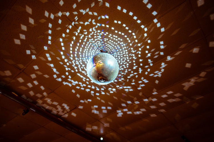 Low angle view of illuminated disco ball hanging from ceiling in nightclub