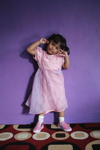 Portrait of cute girl in dress gesturing while standing against wall