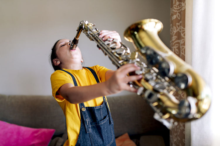 Child with saxophone in living room standing against window in room