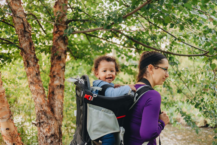 Smiling mother with cute son on back standing on forest