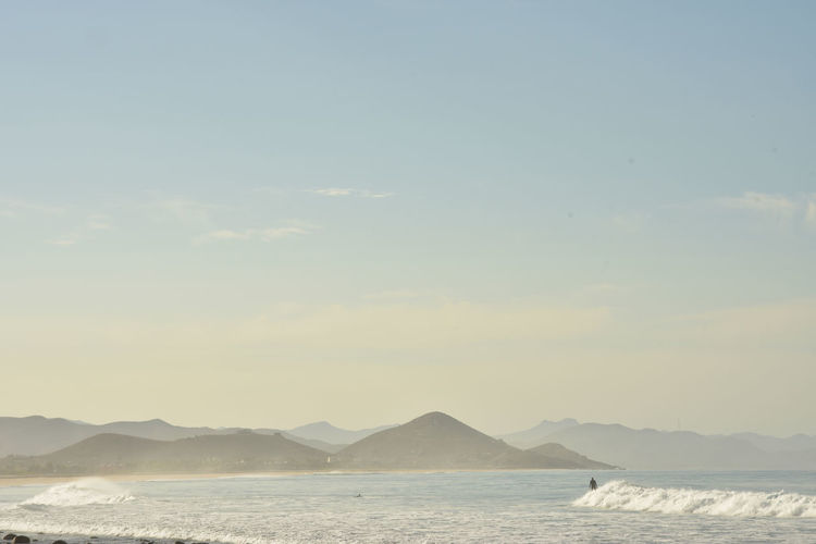 Surfer rides his surf board on a white wave baja, mexico with hills and mountain 