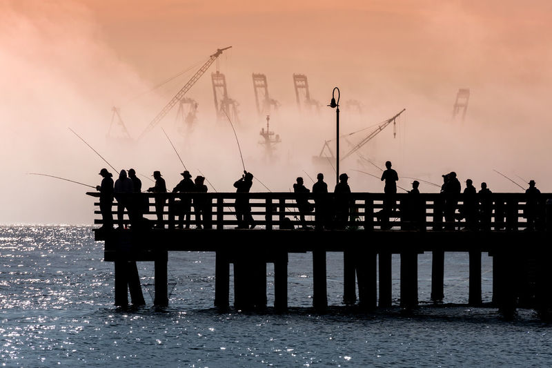 Silhouette people on pier by sea against sky during sunrise