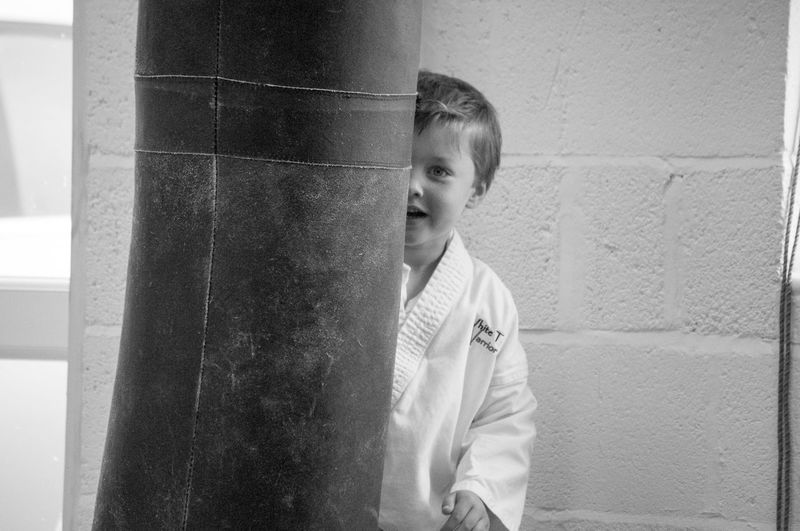 Portrait of boy in sport clothing behind punching bag at martial arts classroom