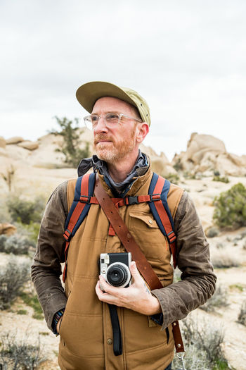 Mature man with glasses and camera in front of desert hill with plants