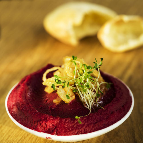 Close-up of beetroot hummus with sprouts in bowl on cutting board