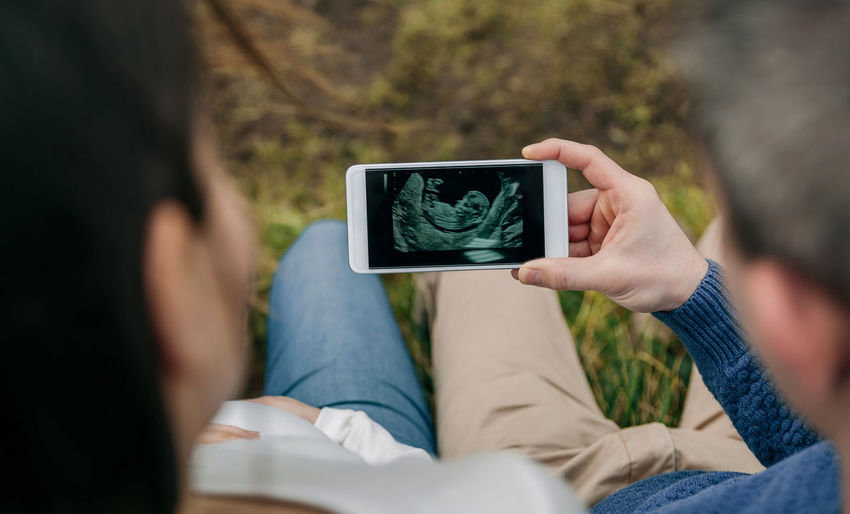 High angle view of pregnant couple watching ultrasound on mobile phone
