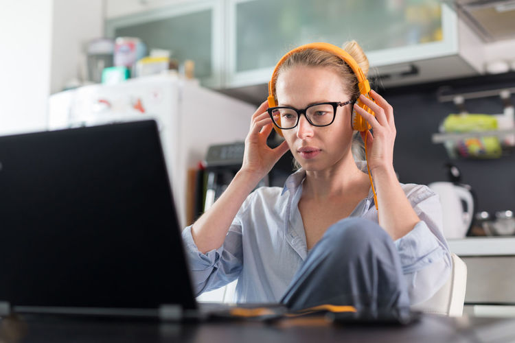 Businesswoman wearing headphones working on laptop at home