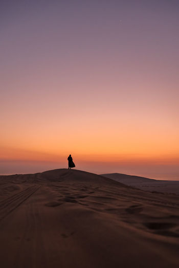Silhouette woman standing on sand dune against sky during sunset