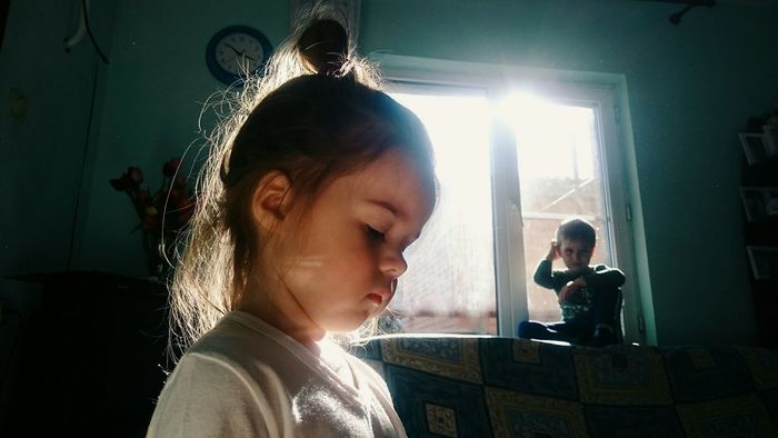Close-up of girl with boy sitting by window at home