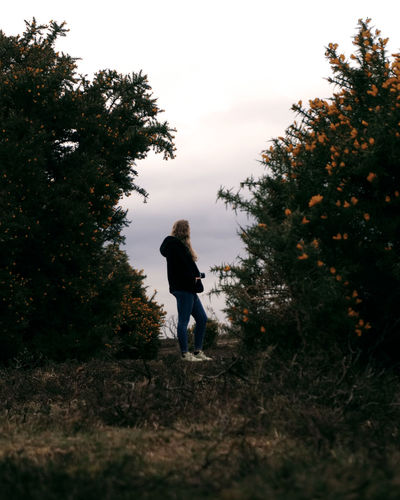 Rear view of woman walking on street amidst trees against sky