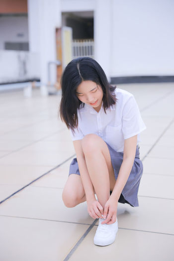 Young woman tying shoelace while sitting on tiled floor