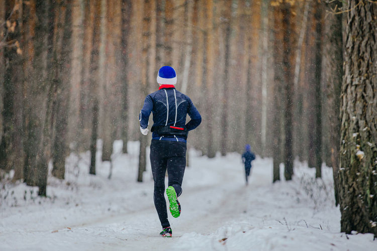 Male runner run winter race in forest on snowfall