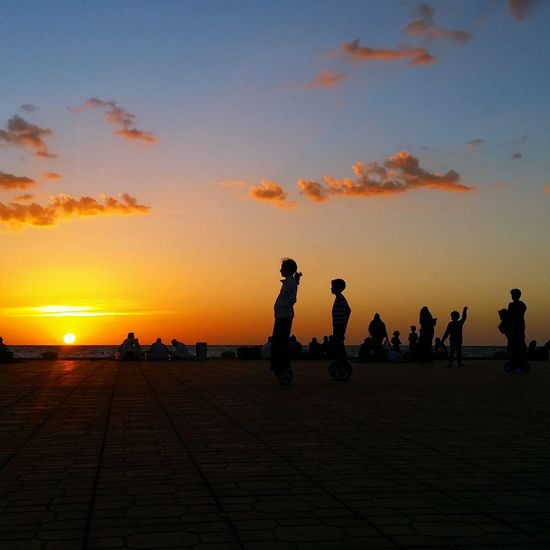Children riding segway by sea against sky during sunset