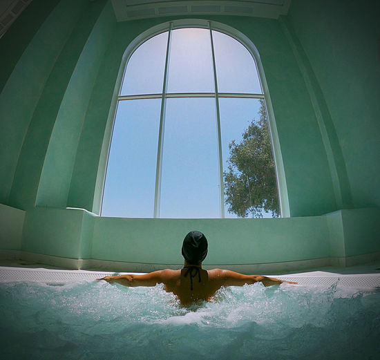 Relaxed woman in swimming pool in front of a window. 