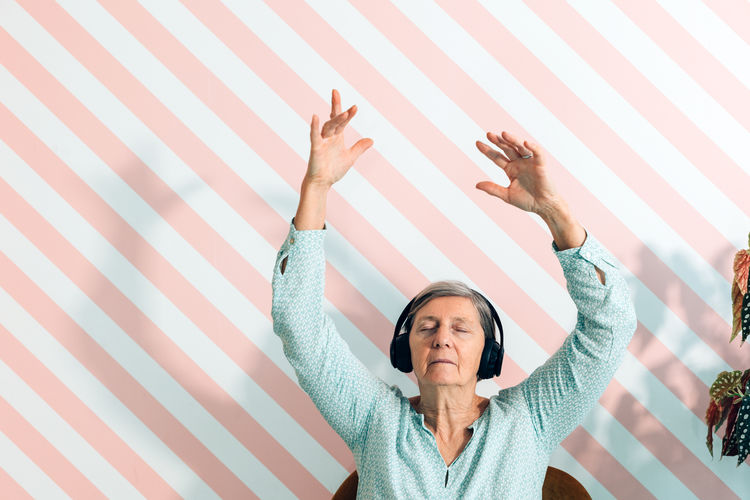 Elderly lady in her seventies listens to music with headphones moving her arms in the air