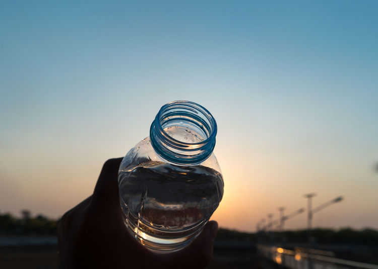 Cropped image of person holding bottle during sunset