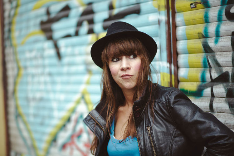 Woman wearing hat against graffiti shutter in city