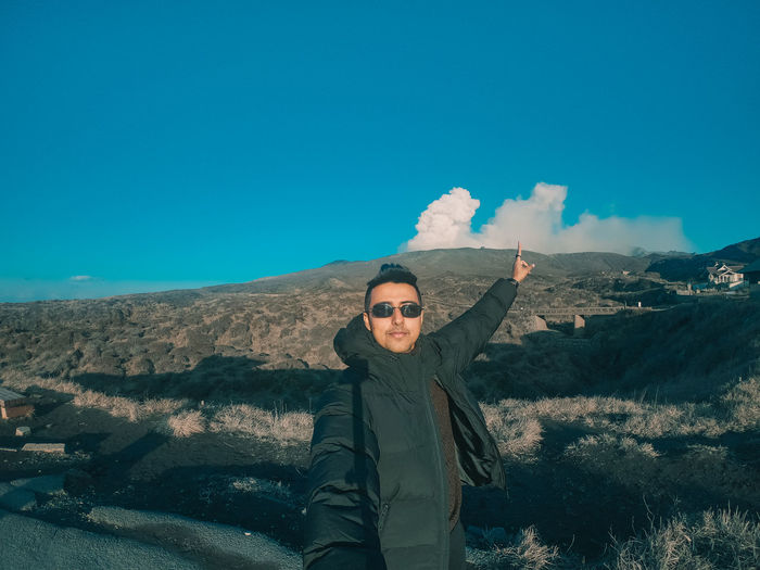 Portrait of young man standing on mountain against sky