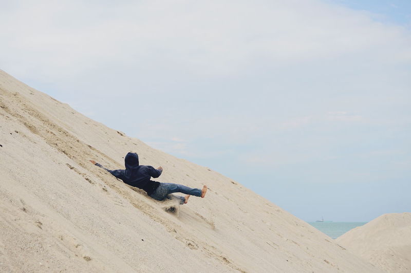 Man falling on sand at beach against sky