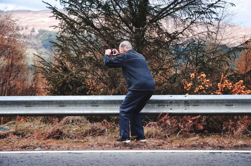 Man photographing while standing by tree against plants