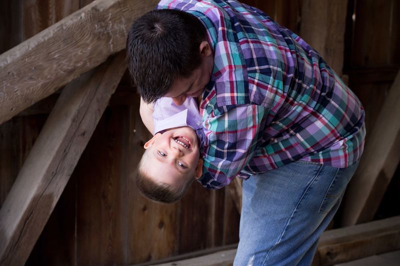 Playful father carrying son while standing against wooden wall