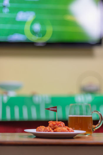 Plate of spicy boneless wings and large glass mug of beer in front of tv watching football game