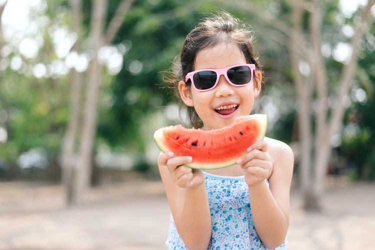 Girl holding watermelon against trees
