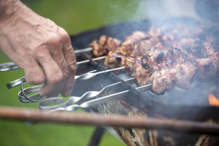 Cropped hand of man preparing meat on barbecue grill