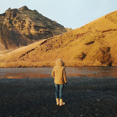 Rear view of woman standing at lakeshore against mountain