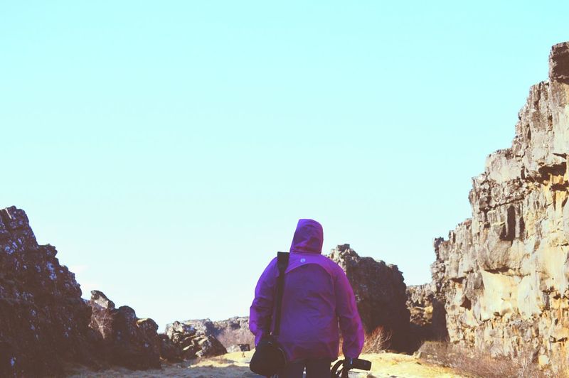 Rear view of woman walking on rocks against clear blue sky