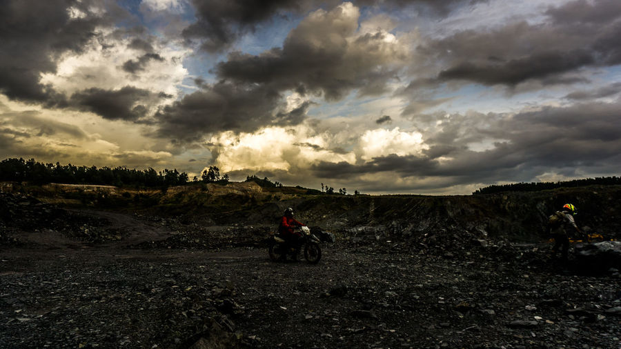 People riding motorcycle on land against cloudy sky