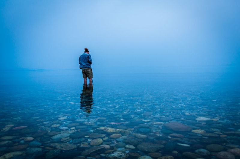 Rear view of man standing in sea against blue sky