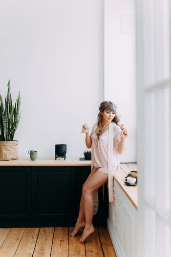 A beautiful girl in pajamas prepares breakfast and pours coffee near the window of the house