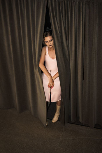 Young woman looking away while standing behind curtain