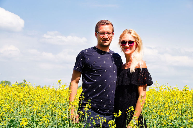 Portrait of smiling couple standing on oilseed rape field