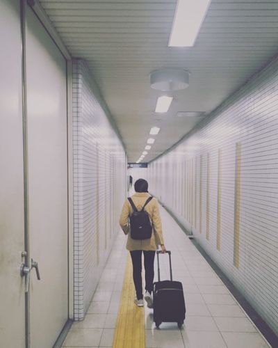 Rear view of woman walking with suitcase in corridor