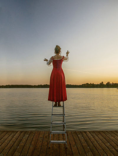 Rear view of woman standing on pier over lake against sky