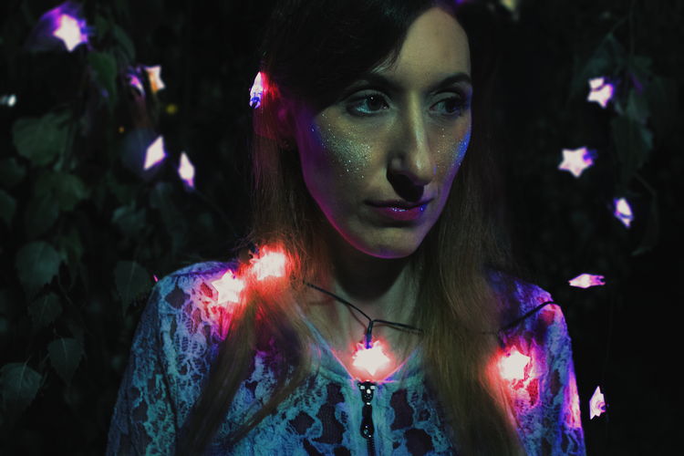 Close-up of woman amidst illuminated string lights at night