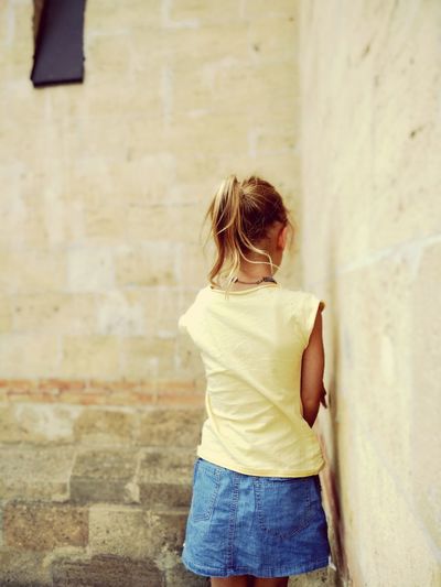 Rear view of girl standing against wall