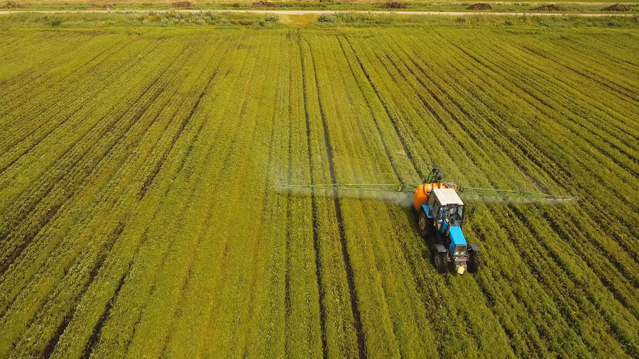 Aerial view tractor spraying the chemicals on the large green field. 