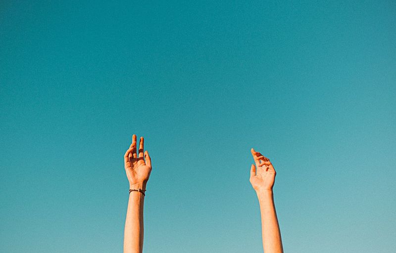 High section of hands reaching against blue sky