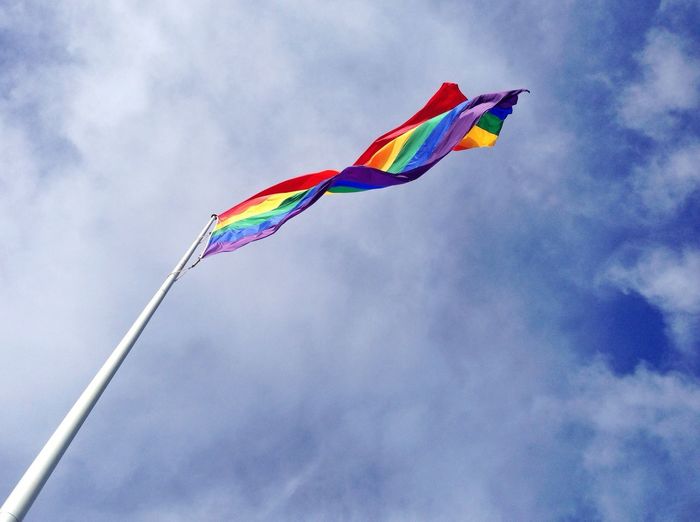 Low angle view of rainbow flag against cloudy sky