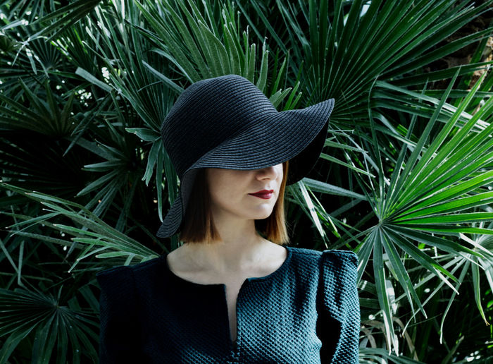 Close-up of woman wearing hat standing against plants