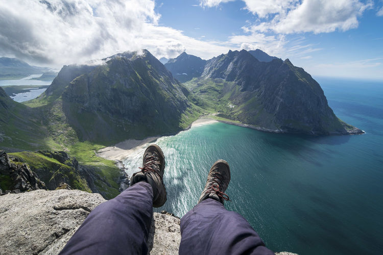 Low section of man sitting on cliff against sea at beach