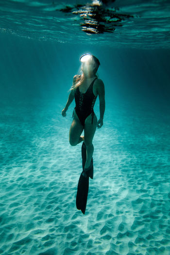 Slim female in swimsuit and flippers swimming underwater in turquoise sea