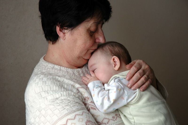 Grandmother carrying sleeping grandson against wall