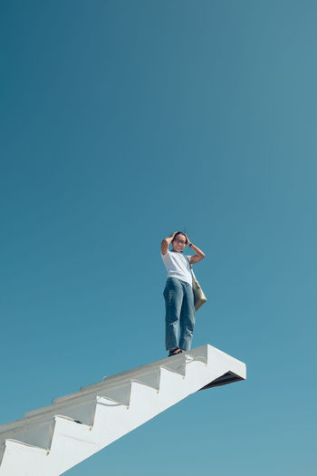 Low angle view of woman standing against clear blue sky