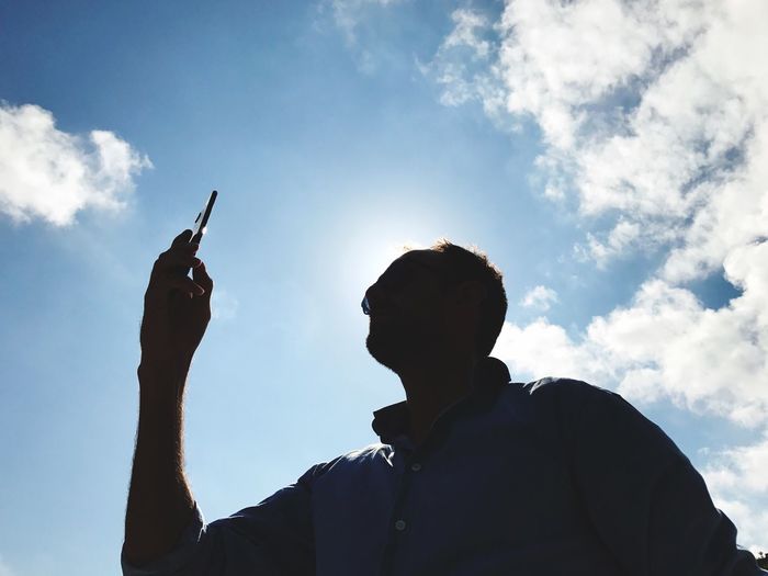 Low angle view of silhouette man using smart phone against sky