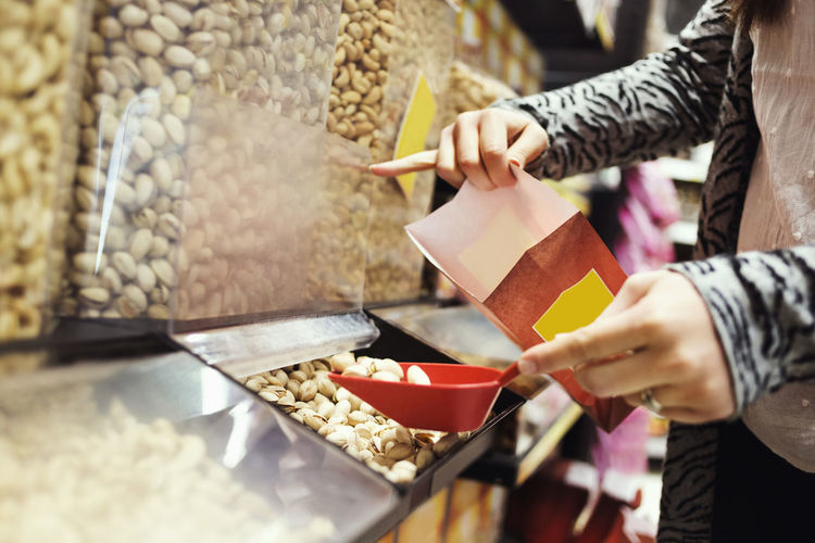 Midsection of woman filling pistachio nuts in paperbag at supermarket