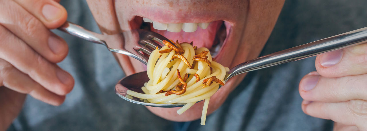 Midsection of man eating noodles and worms in restaurant